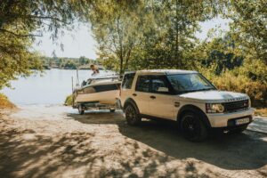 A Land Rover towing a boat to a scenic lakeside under a sunny sky.